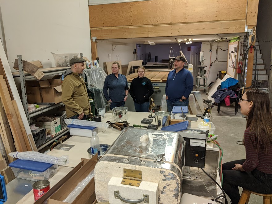 John stands to the left of the torch table talking to the class: a family of three and a single student on the far right.