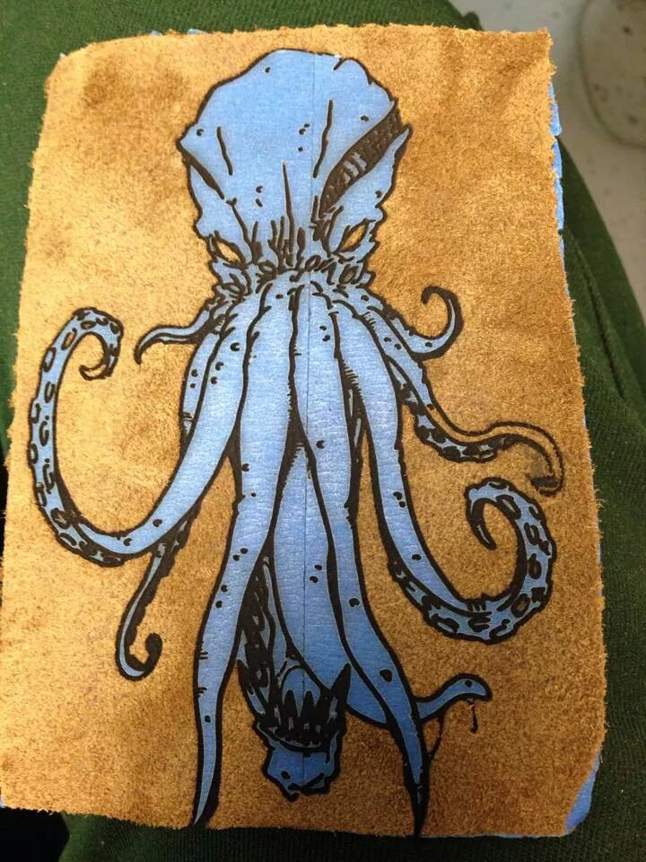 A picture of the finished piece: a blue cthulhu set on top of the hide side of a swatch of leather.