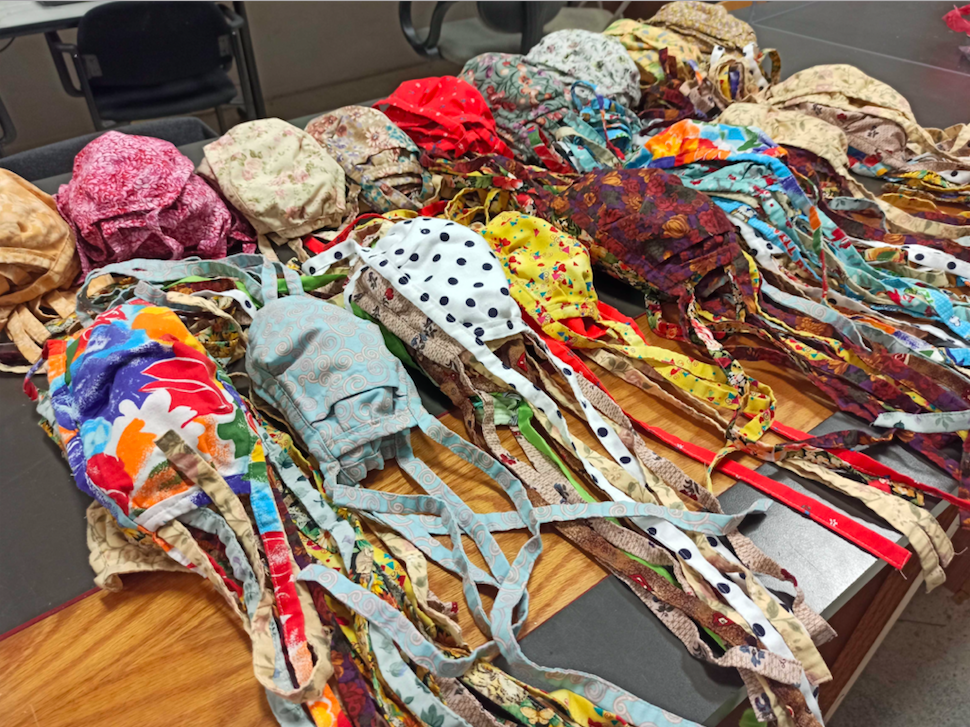 A picture of hundreds of finished masks on Anchorage Makerspace's countertop in a variety of colors, prints, and patterns!